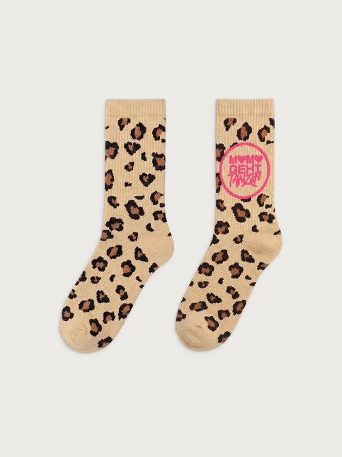 Beige Crew-Socken mit Leopardenmuster in Braun und Schwarz. Auf einer Socke befindet sich ein pinker Kreis mit der Aufschrift „MAMA GEHT TANZEN“. Beide Socken sind frontal auf hellgrauem Hintergrund dargestellt.