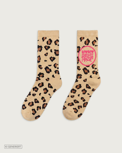 Beige Crew-Socken mit Leopardenmuster in Braun und Schwarz. Auf einer Socke befindet sich ein pinker Kreis mit der Aufschrift „MAMA GEHT TANZEN“. Beide Socken sind frontal auf hellgrauem Hintergrund dargestellt.